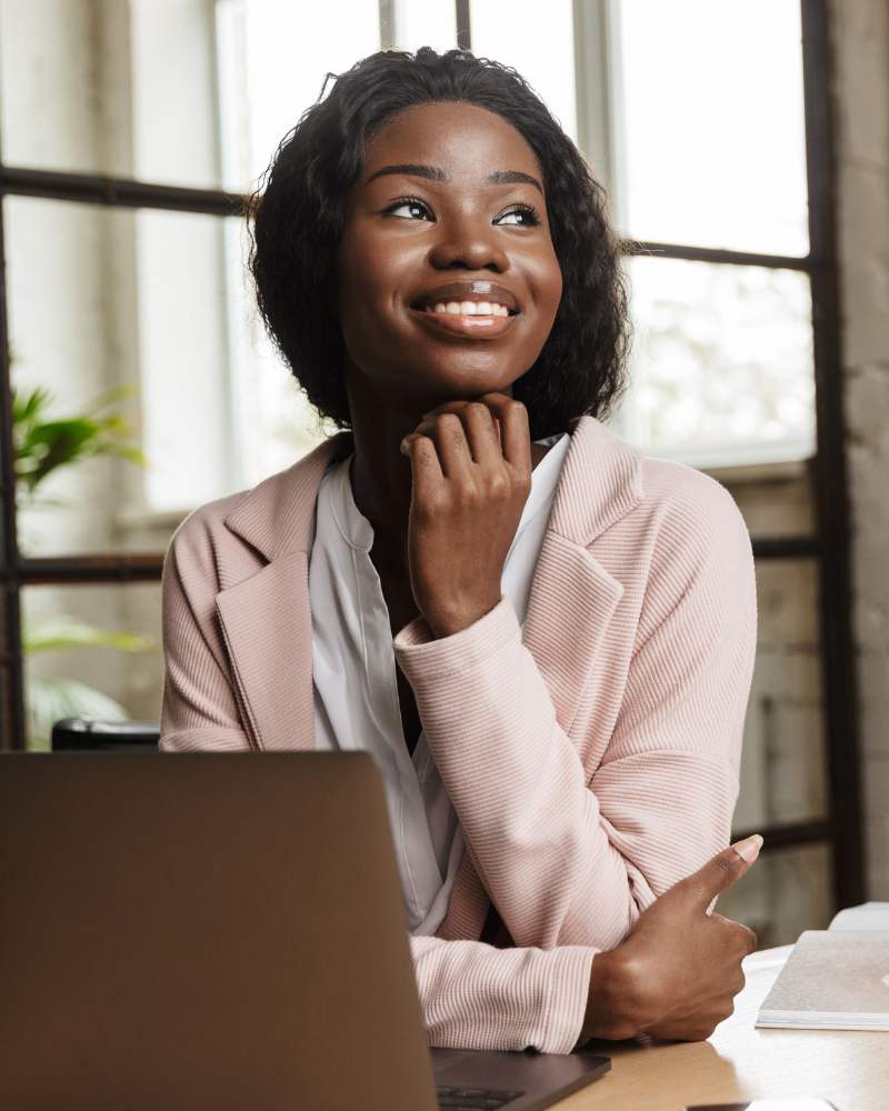 A woman smiling next to computer with great straight teeth thanks to treatment from smiles club.